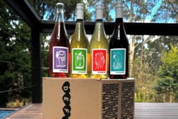 Four bottles of Defialy wines with bright coloured labels, resting on a box on an outdoor deck.