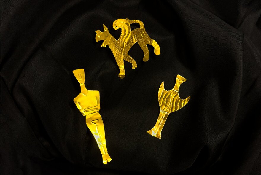 Three gold trinkets on a black background. 