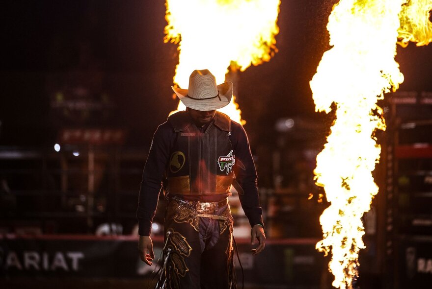 A man dressed as a cowboy in a big hat walking away from two flares. 