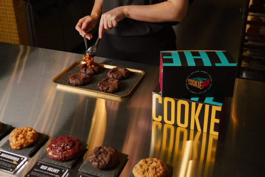 Hands placing cookies onto a tray next to a branded box.
