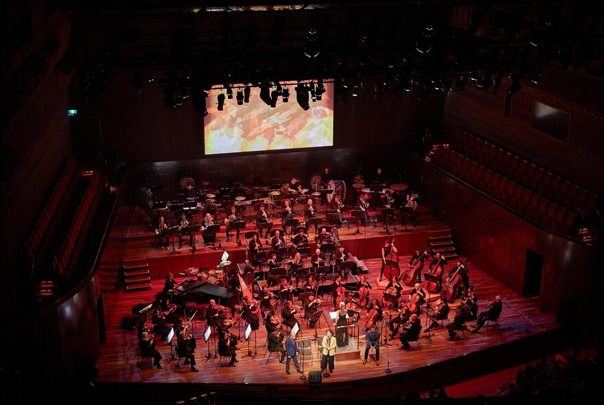 A symphony orchestra performing on a stage in front of a large video screen. 