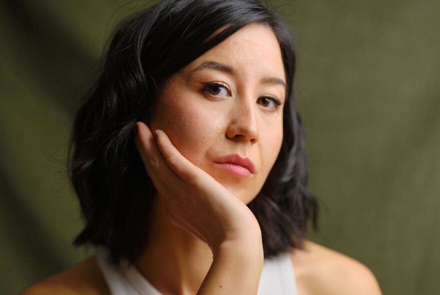 Nina Oyama, posing with her chin on her hand, wearing a white dress.
