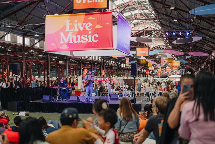 Crowds in a Queen Victoria Market shed with signage and stalls.