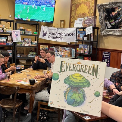 People playing boardgames at tables in a pub room with sport on a large screen.