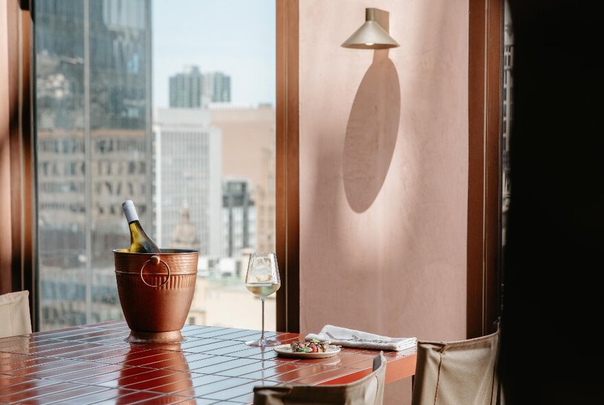 An ice bottle and glass on a bench in a restaurant with upper-level city views.