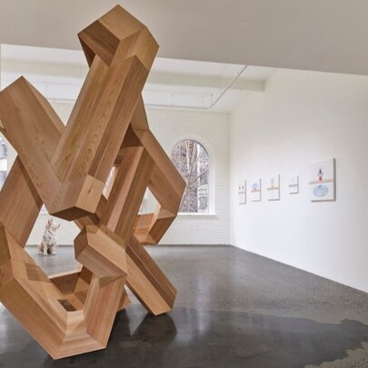 A monumental carved wooden sculpture on display in a gallery setting.