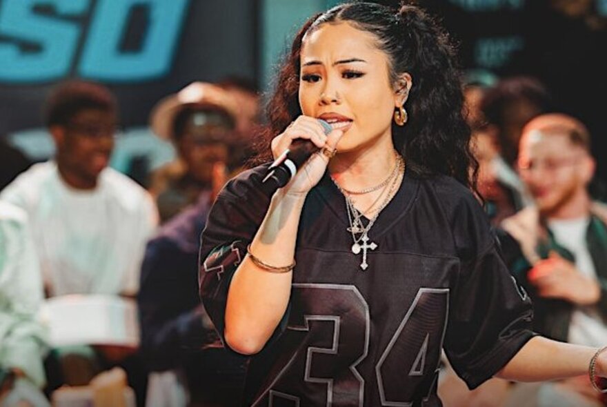 A young singer wearing a black basketball t-shirt, singing into a microphone at a basketball competition.