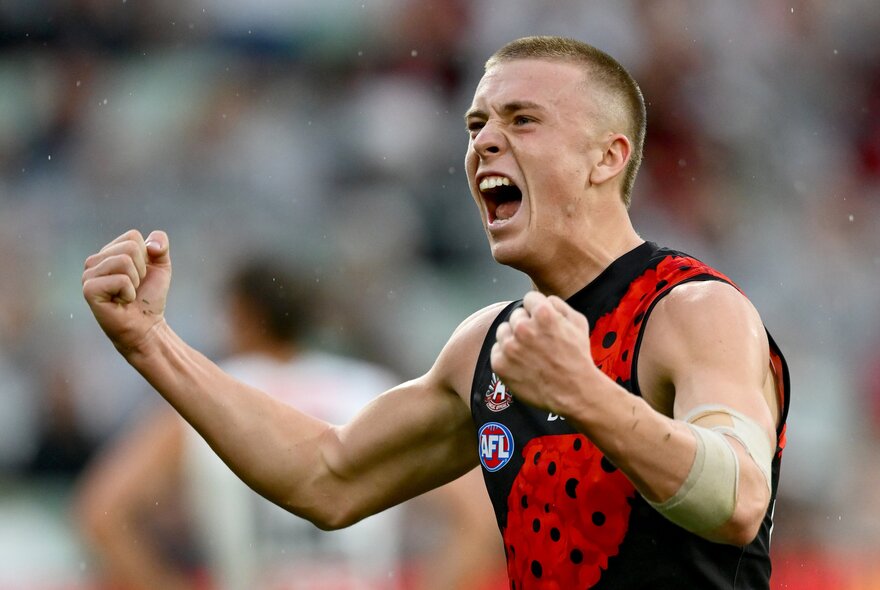 An Essendon AFL player cheering himself on with pumped fists, on the footy field.