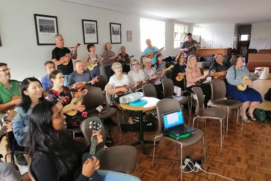 Ukulele group seated with instruments in a community hall setting.