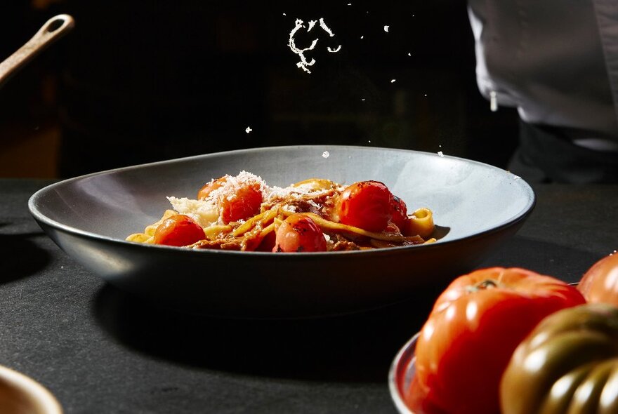 A shallow grey bowl of pasta on a dining table.