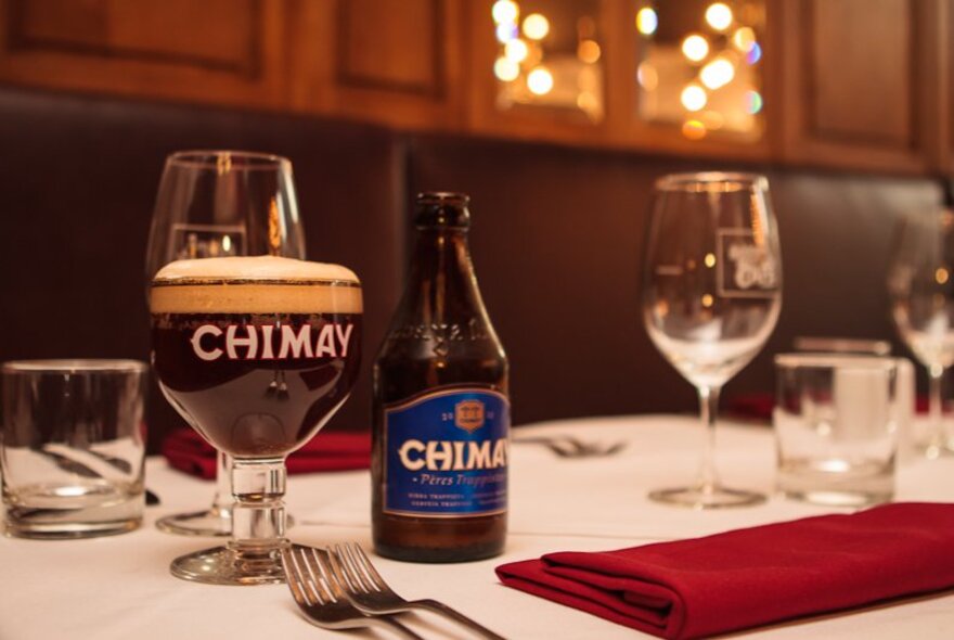 A table set for dinner, with a Belgian beer bottle next to a poured beer in a specialised beer glass.