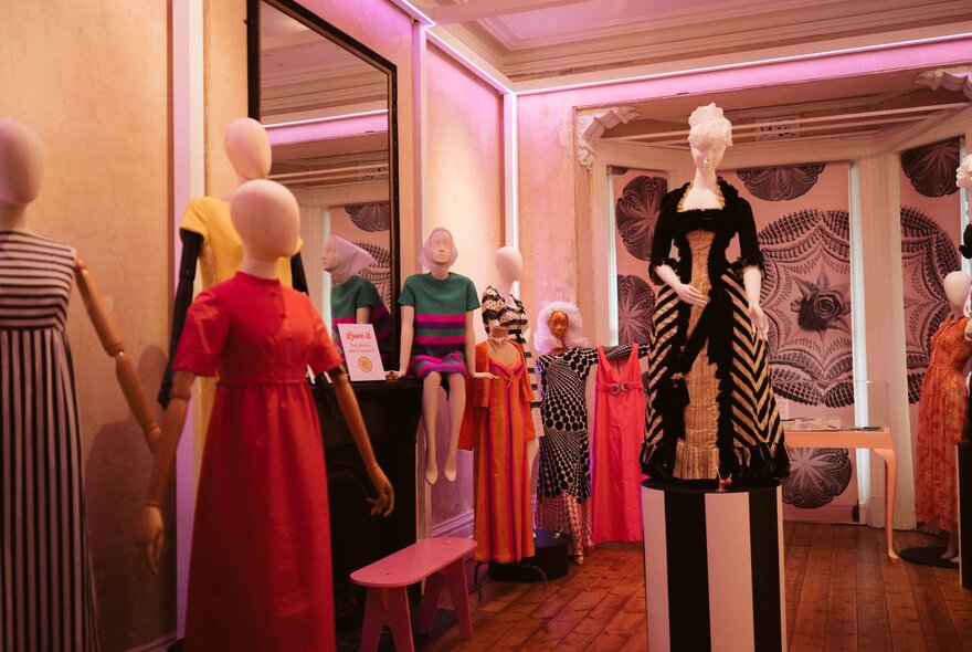 Colourful and bold dresses on faceless clothing mannequins, in an exhibition room.