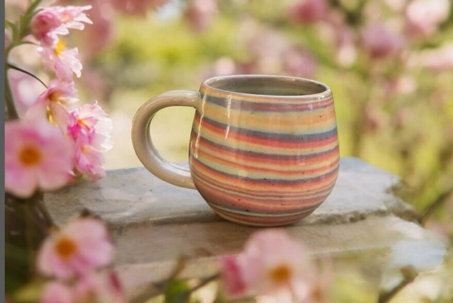 A striped clay mug on a stone next to cherry blossom.