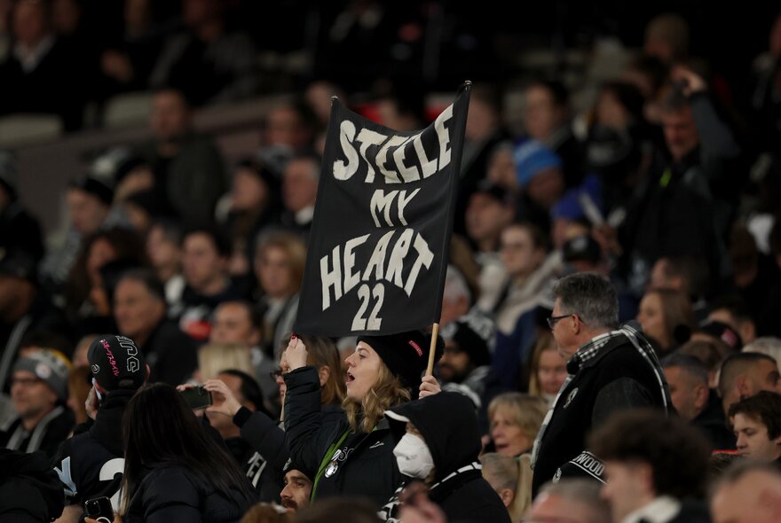 Looking in the Collingwood fan area in a football crowd, a banner raised. 