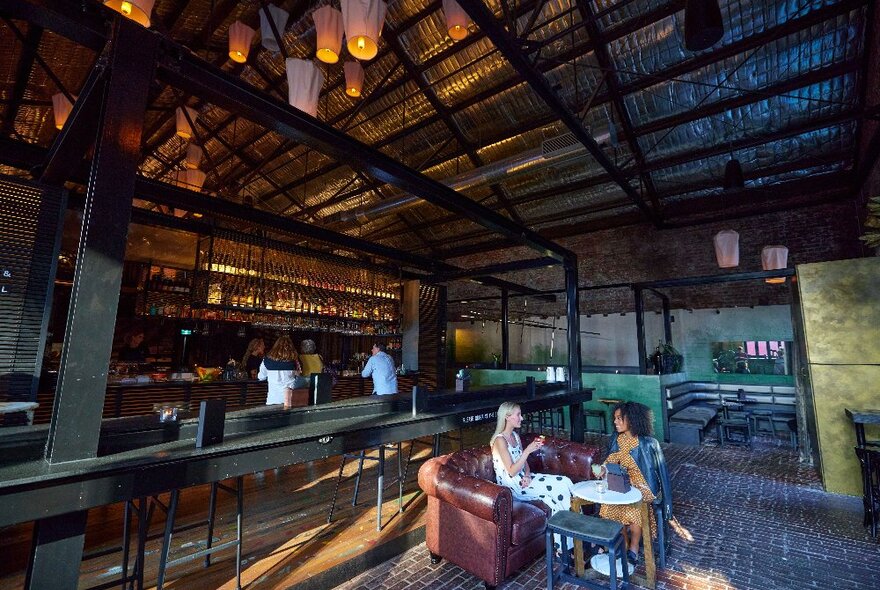 Two people enjoying cocktails in a large open space bar with lanterns hanging from the ceiling above.