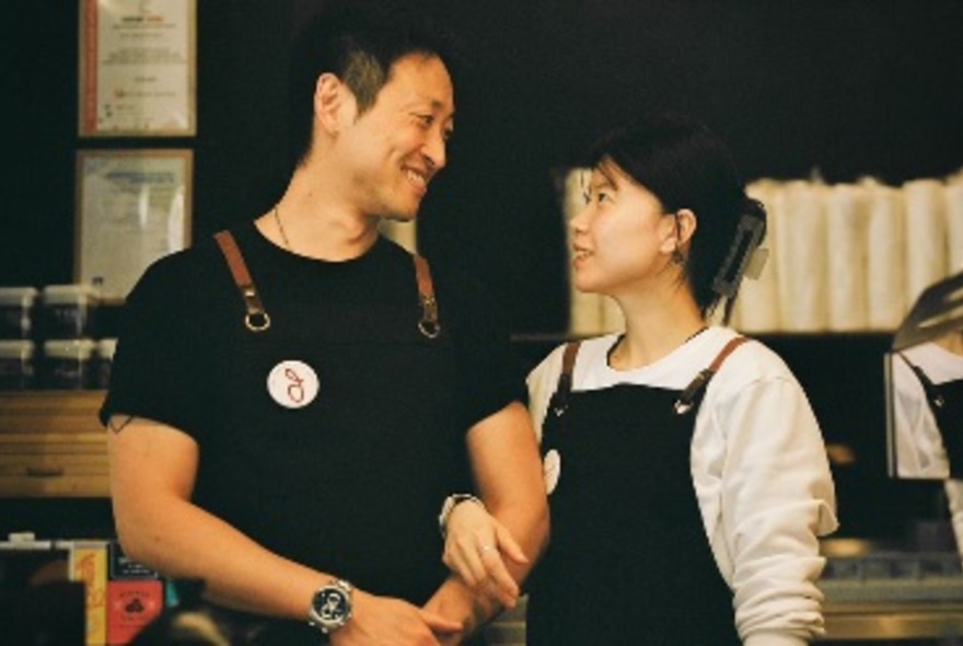 The owners of Cafe Belt Melbourne, with linked arms smiling and looking at each other.