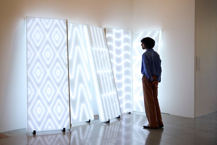 A man is looking at a neon artwork in a gallery.