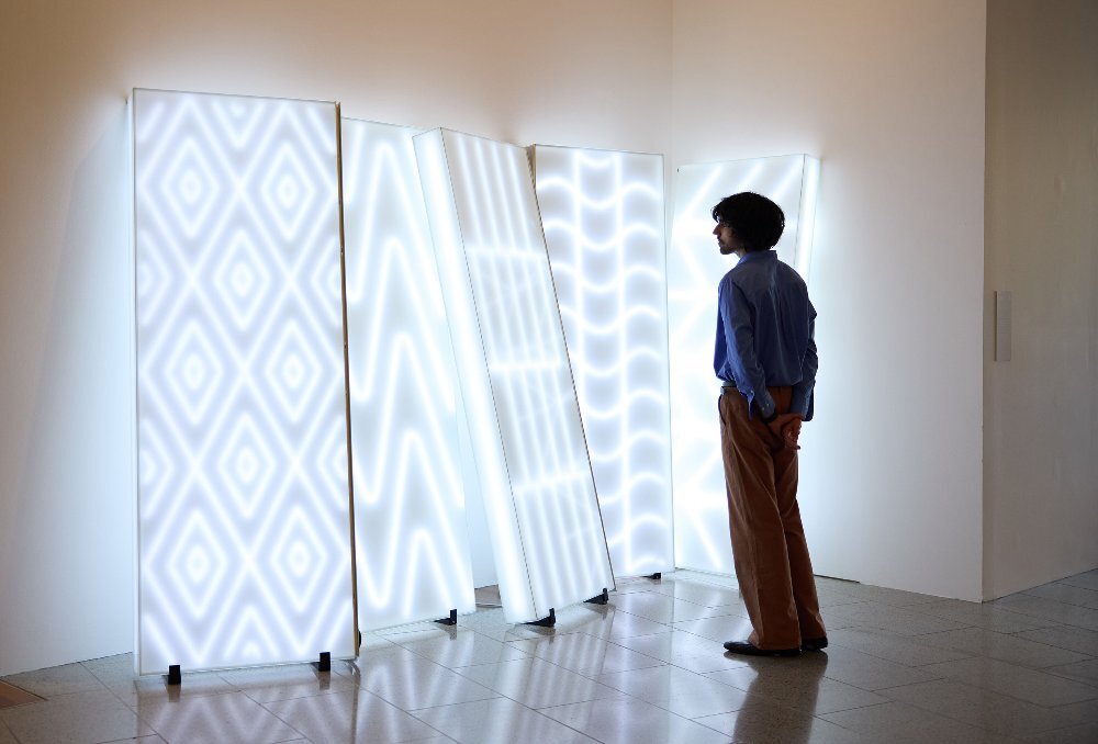 A man is looking at a neon artwork in a gallery.