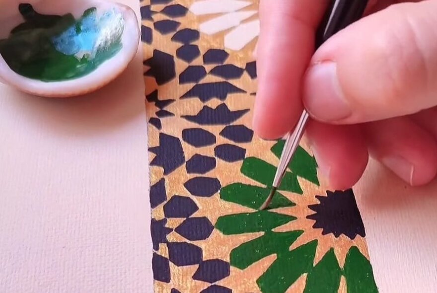 A hand painting a flower petal in green with a very fine brush. 