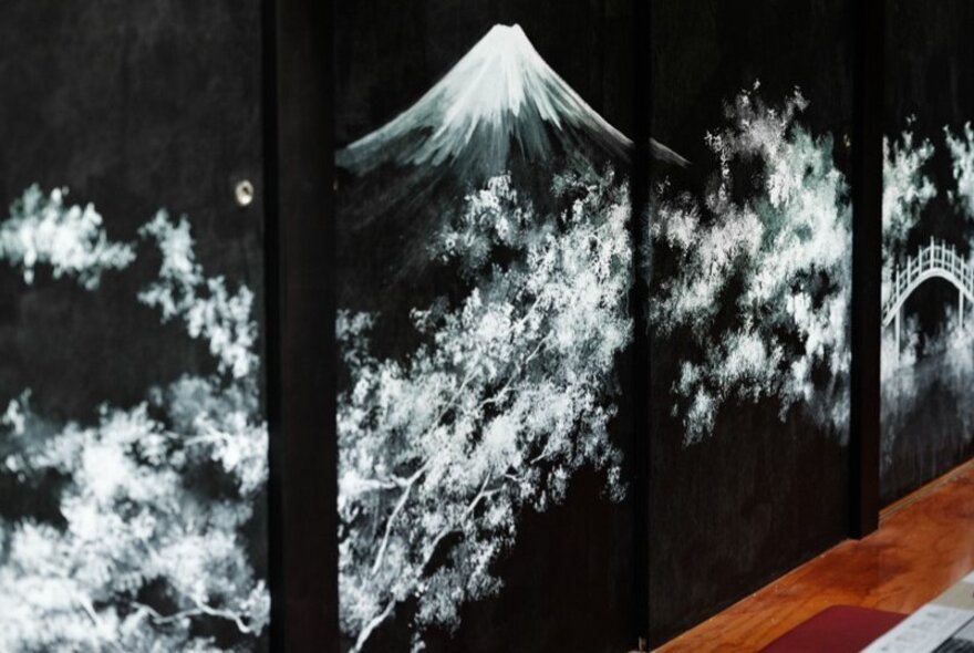 A white fresco painted on black Japanese screens, depicting cherry blossoms in front of Mount Fuji. 