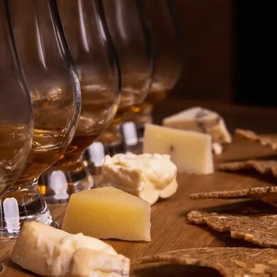 A sample of five whiskey pours with a small chunk of cheese and a cracker in front of each glass.