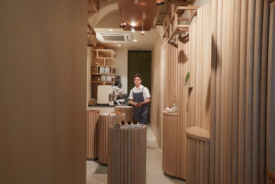 View into a small bakery cafe, showing curved panelled walls and a man in a long chef's apron standing behind a counter.