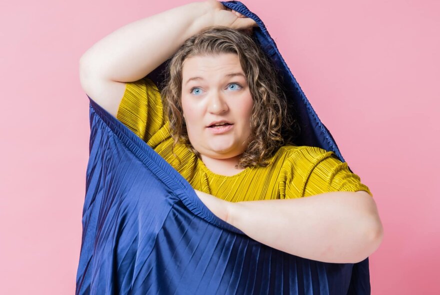 A woman climbing out of a sack or sleeping bag, with one hand supporting the fabric above her head.