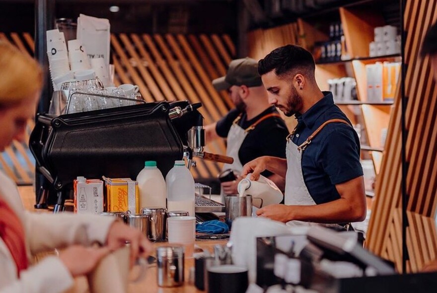 Staff behind café counter making coffees.