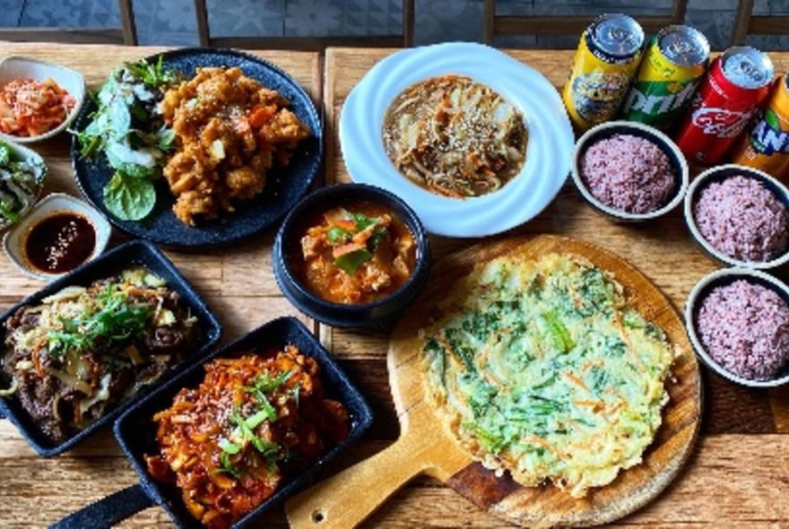 Looking down at a table laden with different Korean dishes and soft drinks. 