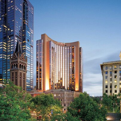 A view of the Melbourne skyline at dusk, showing the Grand Hyatt Melbourne with peachy lights and a cathedral spire on the right. 