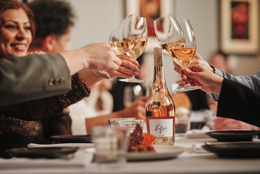 People seated around a table bringing their glasses of rose in for a toast. 
