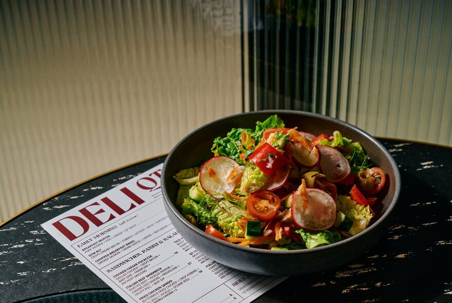 Bowl of salad on a cafe table with menu.