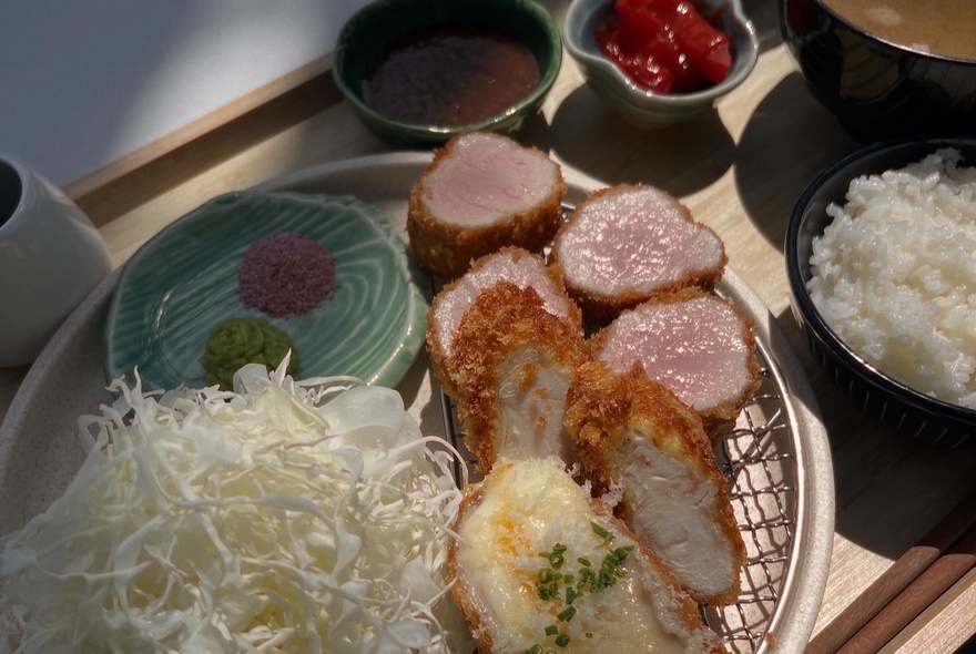  Crumbed katsu on a wire tray with dipping sauce, shoots, rice and condiments.