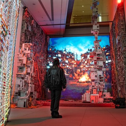 Person standing in an exhibition gallery with digital and sculptural displays.