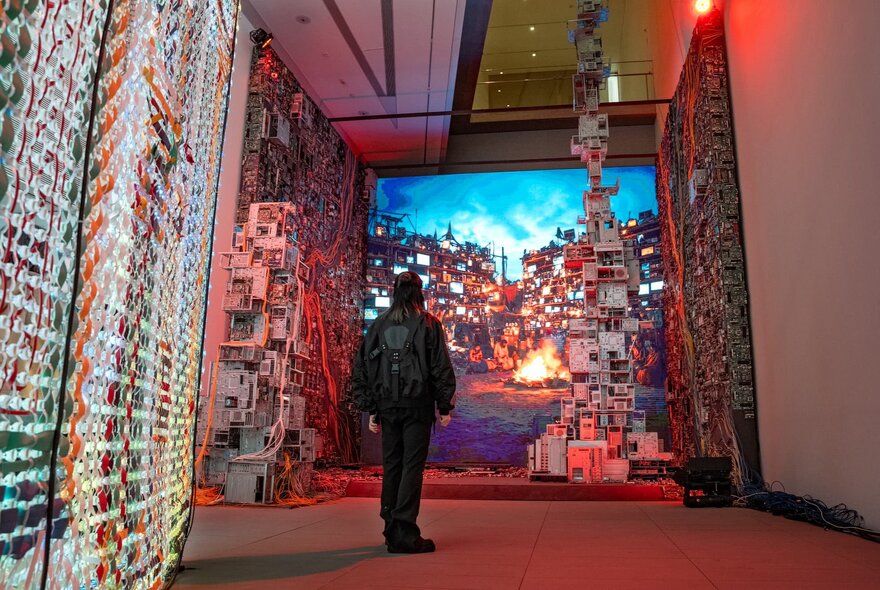 Person standing in an exhibition gallery with digital and sculptural displays.