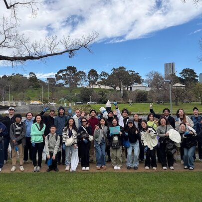 Group of people standing beside the Yarra River with a bridge in the background.