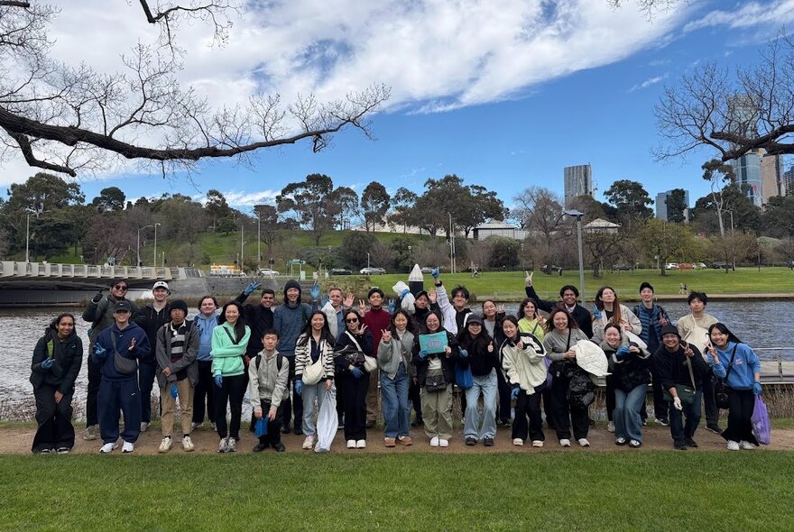 Group of people standing beside the Yarra River with a bridge in the background.