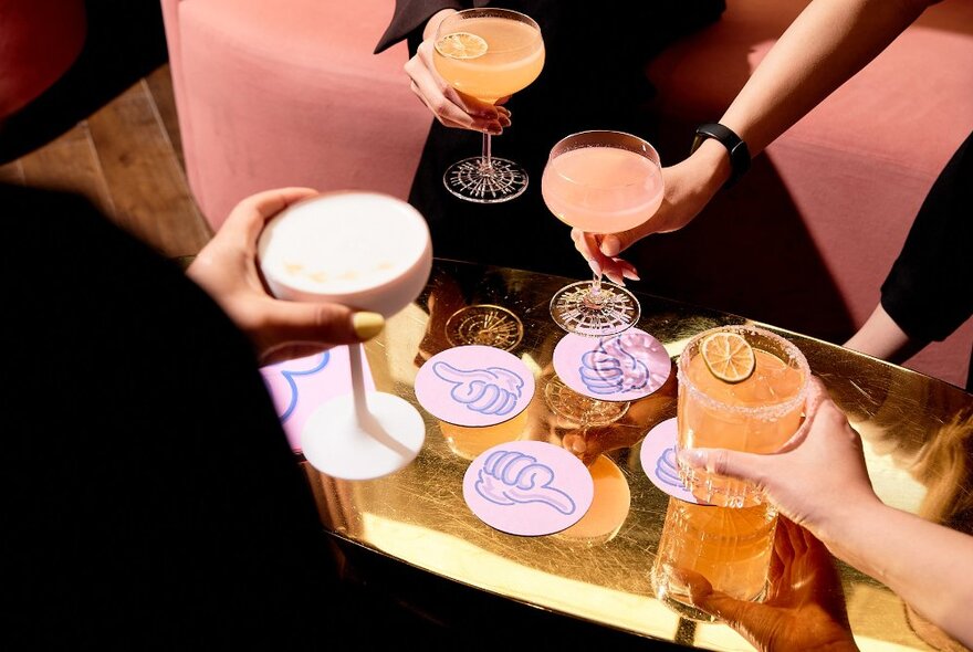Hands picking up cocktails off coasters from a low table.