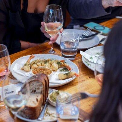 A table in a restaurant with plates of food mid-meal, bread and glasses of wine.