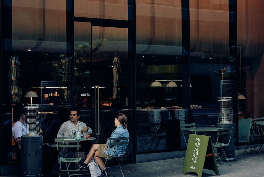 Diners seated at an outdoor table outside the windows of Greta restaurant.