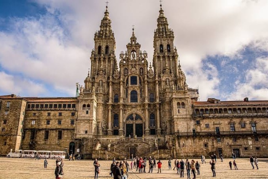 Cathedral of Santiago de Compostela in Galicia, Spain - an imposing structure with a large piazza in the foreground and many people walking around.