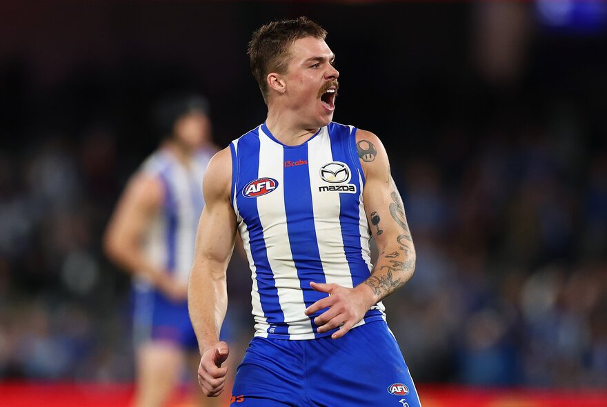 A North Melbourne AFL football player cheering and looking pumped during a match.