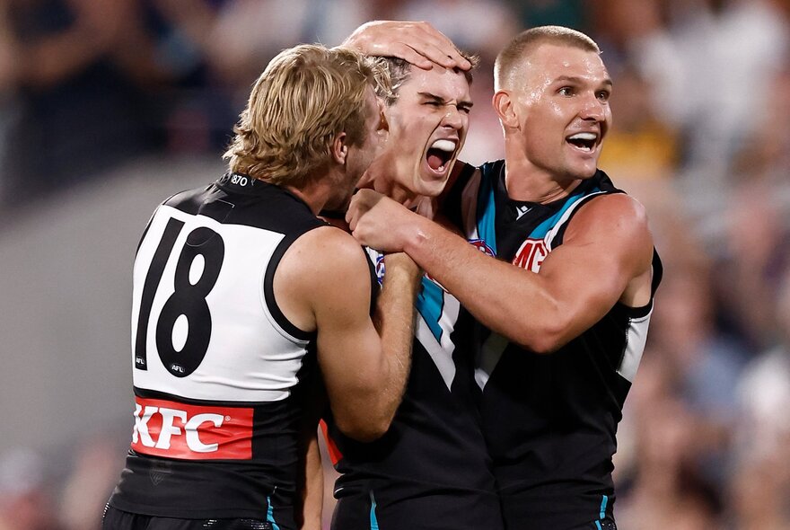 Three Port Adelaide AFL players celebrating on the field.