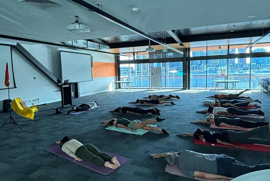 People laying face down indoors on yoga mats.