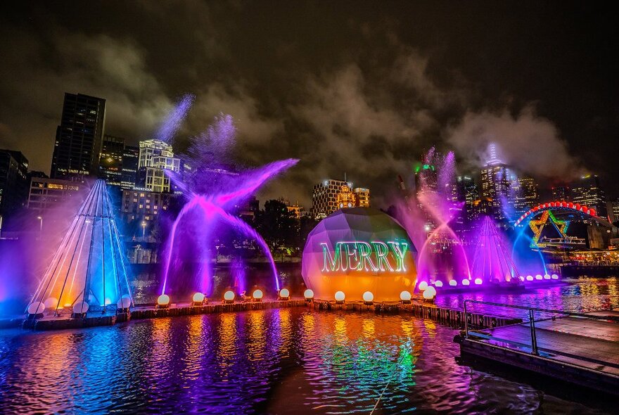 A light show with giant baubles and water squirting on a river at night.