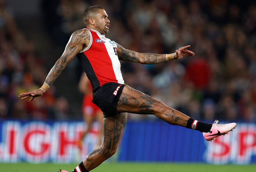 A St Kilda player with leg extended and arms out during a football match.