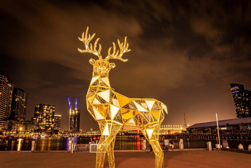 A large golden sculpture of a reindeer in the city at night.