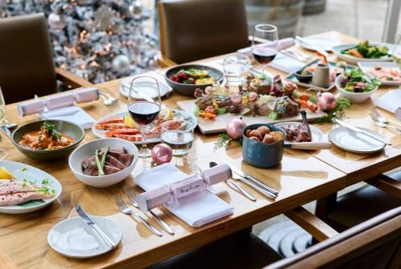 A table in a restaurant filled with plates of festive, seasonal food, and Christmas decorations.