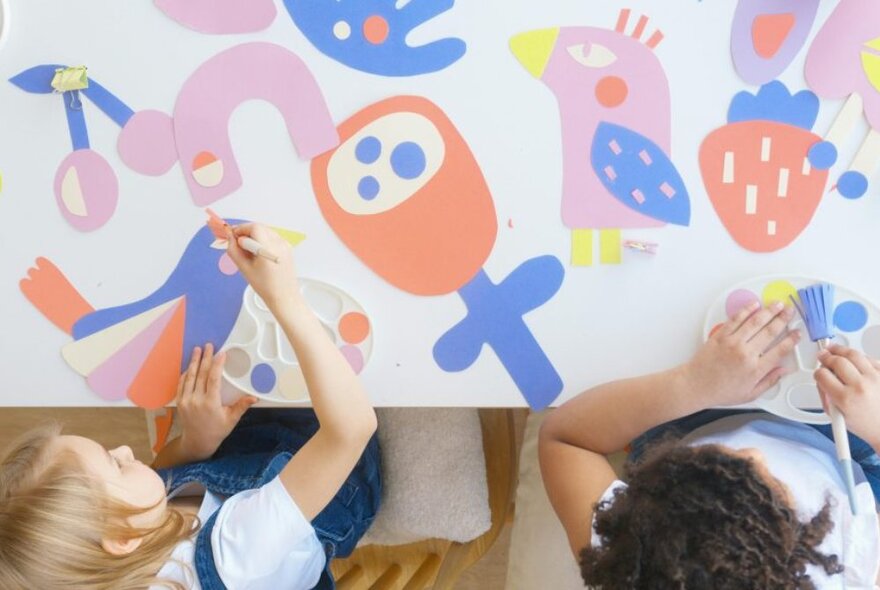 Two children painting at a craft table with paints and brushes.