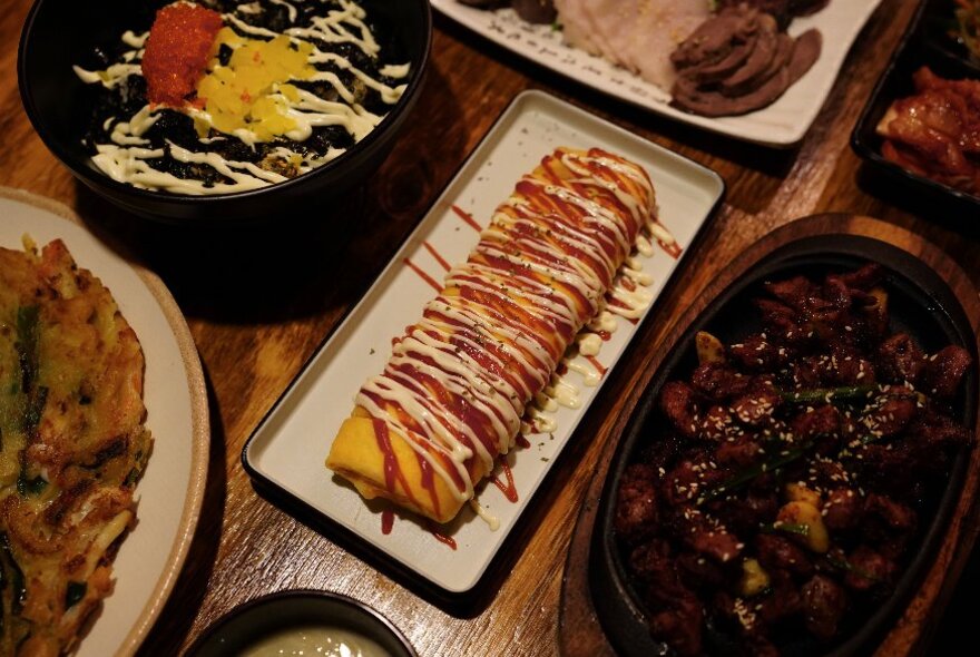 A Korean egg roll, presented on a white platter with other Korean delicacies on plates surrounding it.